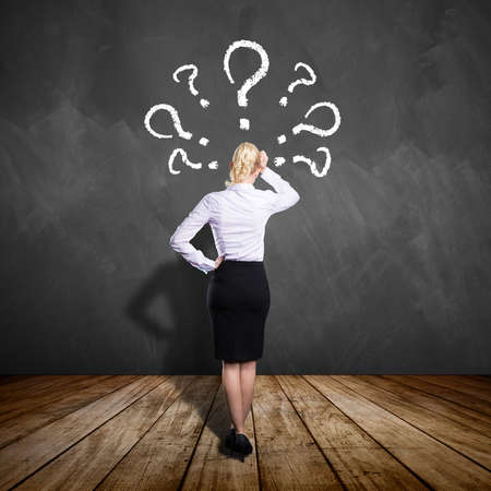 businesswoman thinking about a problem in front a chalkboard with many questionmarksの写真素材