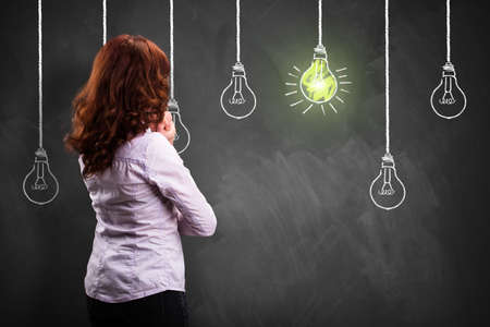 businesswoman standing in front of a blackboard with drawn lightbulbs, symbolizing having an ideaの写真素材
