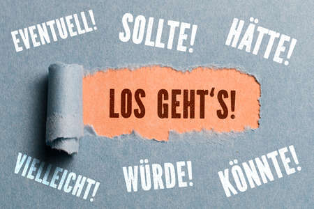 torn paper revealing command "let's go" to procrastinating words surrounding the hole (in German)の写真素材
