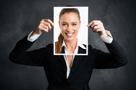 businesswoman holding a picture of herself, showing positive attitude as a facadeの写真素材