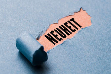 torn paper revealing the word novelty in German