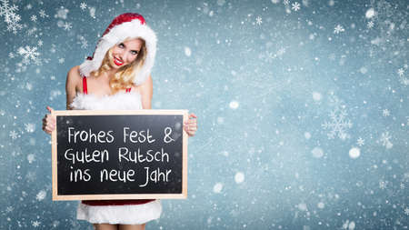 attractive miss santa with a blackboard in a snowy landscape and merry christmas message in Germanの写真素材
