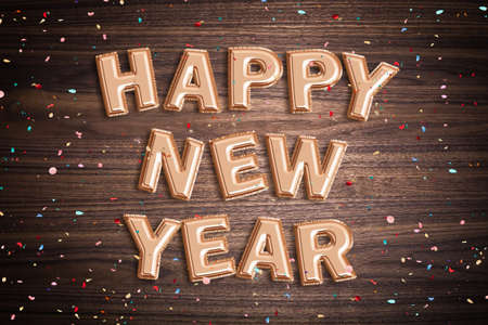 Balloons forming the words "Happy new year" with confetti on wooden surfaceの写真素材