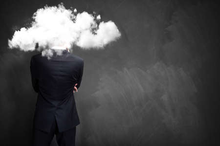 businessman standing in front of a chalkboard with his head in a cloudの写真素材