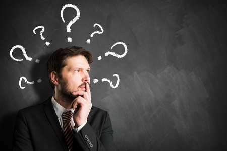 Businessman having many questions symbolized as question marks on a blackboard over his head