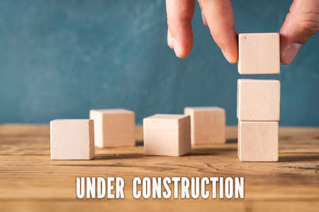 hand is stacking blank cubes and the message "under construction"の写真素材