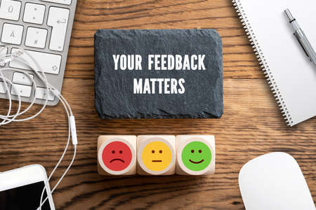 cubes with a emoticons and slate plate with message "your feedback matters" on wooden backgroundの写真素材