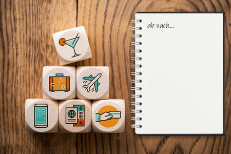 cubes with travel icons and a notebook with the words let's go to in German on wooden background