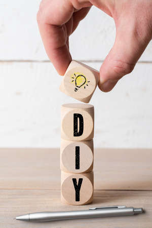 hand is stacking cubes with acronym DIY and an idea symbol on wooden tableの写真素材