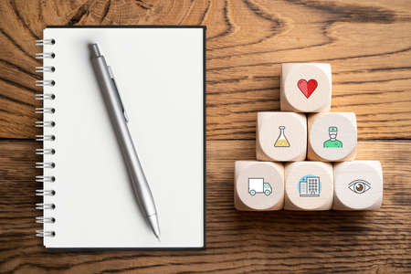 medical icons on cubes with empty note pad on wooden background