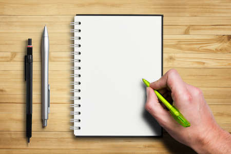 hand starting to write on empty notepad on wooden backgroundの写真素材