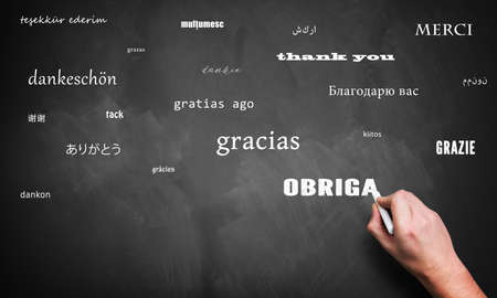 hand is writing the word "thank you" in many languages on a blackboardの写真素材