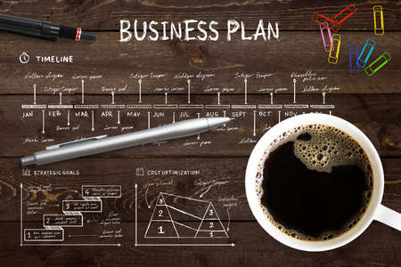 Close-up view from above of a professional desk with a cup full of hot coffee, colored paper clips and a pen on a complex written business plan with copy spaceの写真素材