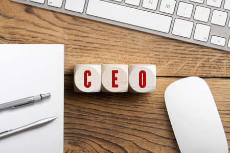 CEO spelled in red on three wooden blocks next to keyboard, mouse and paper with pens on wood surfaceの写真素材