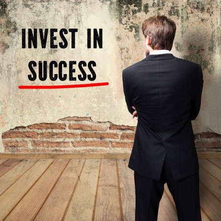 thoughtful businessman standing in front of a wall with the message "Invest in success"の写真素材
