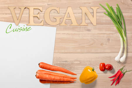 Healthy fresh farm vegetables for Vegan Cuisine arranged on a wooden table with text and sheet of blank white paper with copy spaceの写真素材