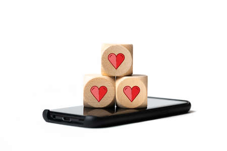 Stack of three wooden blocks with heart icons sitting on smart phone screen over plain white backgroundの写真素材