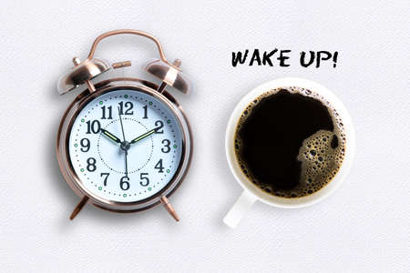 Mug of coffee and classical copper colored alarm clock with bells in a Wake Up concept on a white table with textの写真素材