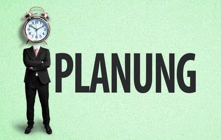 businessman with alarm clock as a head and the German word for "planning" on paper backgroundの写真素材