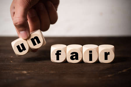 hand is removing two blocks with letters to change the word unfair to fair on wooden backgroundの写真素材