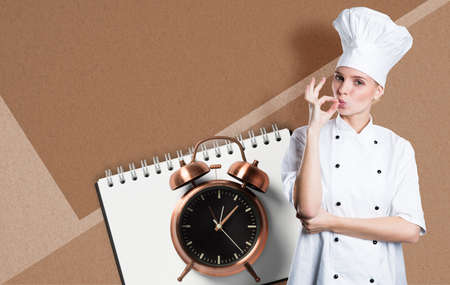woman with a chefs hat in front paper background and alarm clock and notepadの写真素材