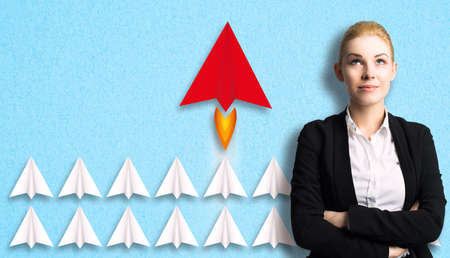 businesswoman having an idea, symbolized by an airplane that is ahead of others in front of paper...