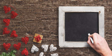 hand over an empty chalkboard surrounded by heart-shaped decoration and a gift on wooden backgroundの写真素材