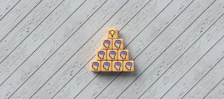 cubes with a lightbulb and person-symbols stacked as a pyramid on wooden background- 3D rendered illustrationの写真素材