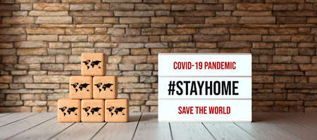 lightbox with message COVID-19 PANDEMIC #STAYHOME and cubes with world map symbols in front of brick...