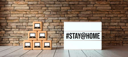 lightbox with message #STAY@HOME and cubes with computer symbols in front of brick wall on wooden...
