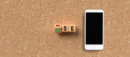 cubes with the text 5G and the option between NO and YES with a smartphone on cork backgroundの写真素材