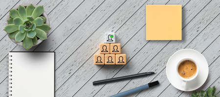 cubes with person-symbols stacked as a pyramid with office items on wooden background