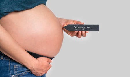 pregnant woman holding arrow with message COMING SOON in front of a grey backgroundの写真素材