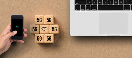 cubes with 5G and WLAN symbol and hand with smartphone and laptop on paper backgroundの写真素材