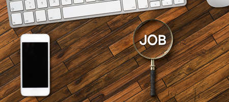 magnifying glass with the word JOB and office equipment on wooden backgroundの写真素材