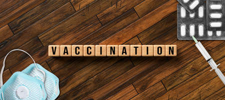 cubes with message VACCINATION and with syringe, face masks and pills on wooden backgroundの写真素材