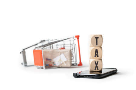 shopping cart laying on the side and cubes with the word TAX on a smartphone isolated on whiteの写真素材