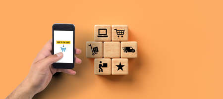 smartphone with message ADD TO CART and cubes with shopping icons on orange background