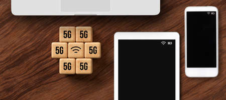 cubes with 5G and WLAN symbol besides tablet, smartphone, and laptop on wooden backgroundの写真素材