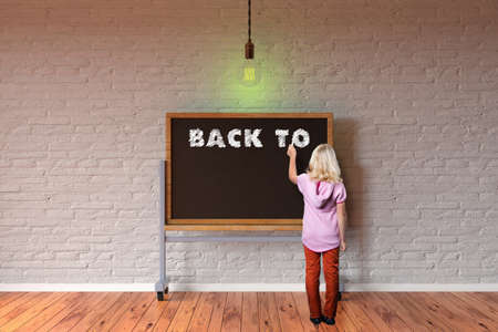 young girl in front of blackboard writing the message BACK TO ...の写真素材