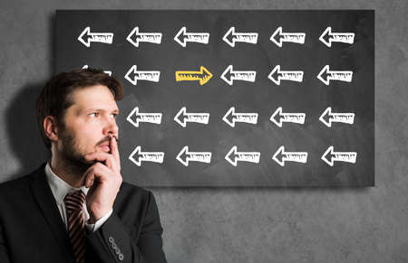 businessman looking in front of a blackboard with an arrow symbol that is different from all others