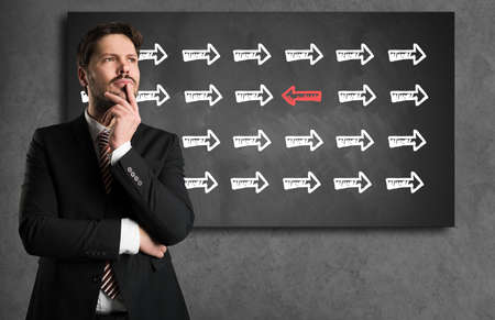 businessman looking in front of a blackboard with an arrow symbol that is different from all othersの写真素材