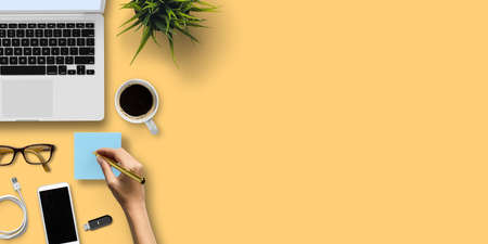 hand with pen over notepad and other office equipment on colorful backgroundの写真素材