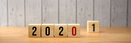 cubes showing the number 2020 and another one with a 1 standing by on wooden background - 3d illustrationの写真素材