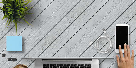 hand over a smartphone with coffee and office equipment on wooden background