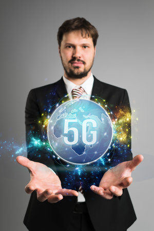 businessman presenting a virtual world map with message 5G in front of grey background