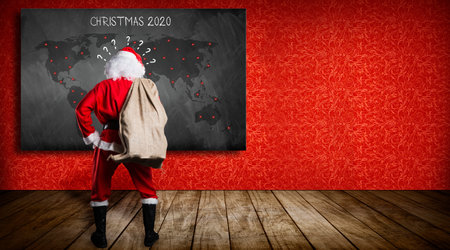 confused santa claus in front of a blackboard with a world map and message CHRISTMAS 2020 on red backgroundの写真素材