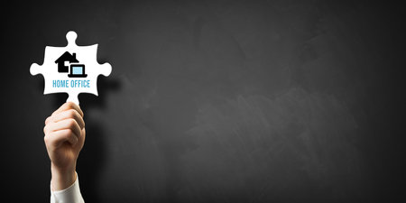 hand holding puzzle piece with message HOME OFFICE in front of a blackboardの写真素材