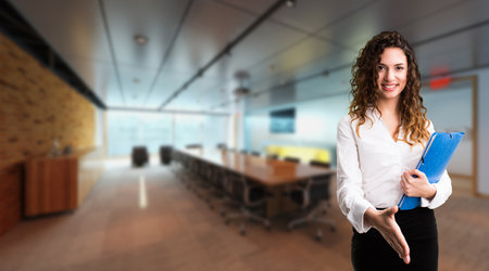 smiling businesswoman ready to shake hands in front of an office scene