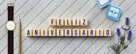 cubes with Spanish message for HAPPY ANNIVERSARY with gifts and flower decoration on wooden...